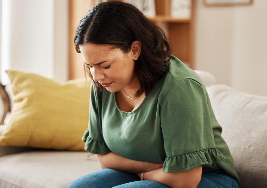 woman on a sofa with stomach pain, grimacing and gripping stomach